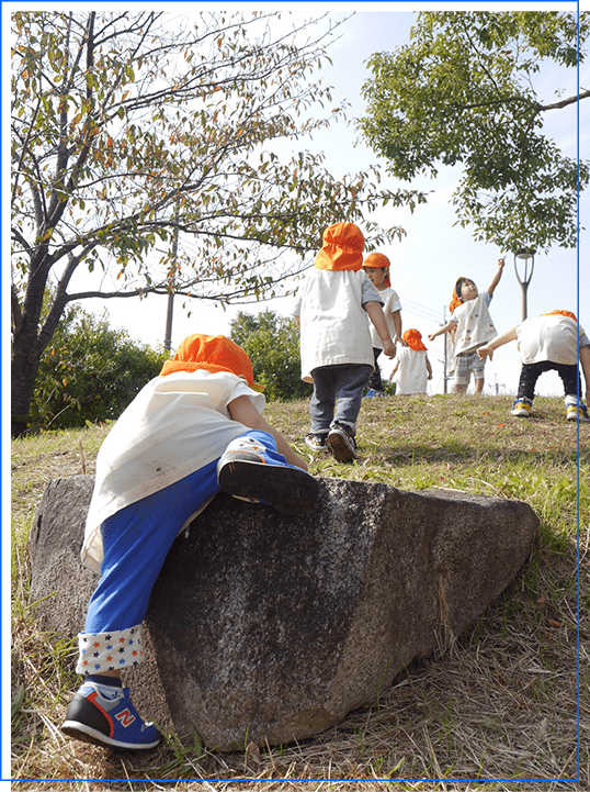 大きな石によじ登る園児